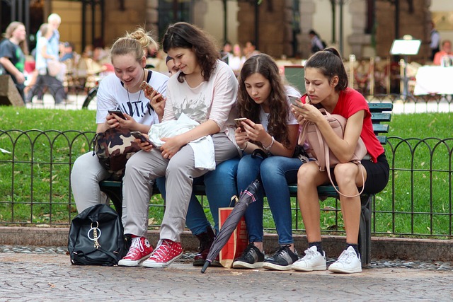 Chicas sentadas en un banco de un parque mirando sus teléfonos móviles.